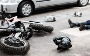 Motorcycle Accidents 9 Overturned motorcycle with a helmet on the ground and an injured person lying in the background after an accident.