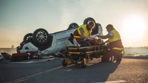 Catastrophic injury 9 Paramedics attending to an injured person on a stretcher beside an overturned vehicle on a road at dusk.
